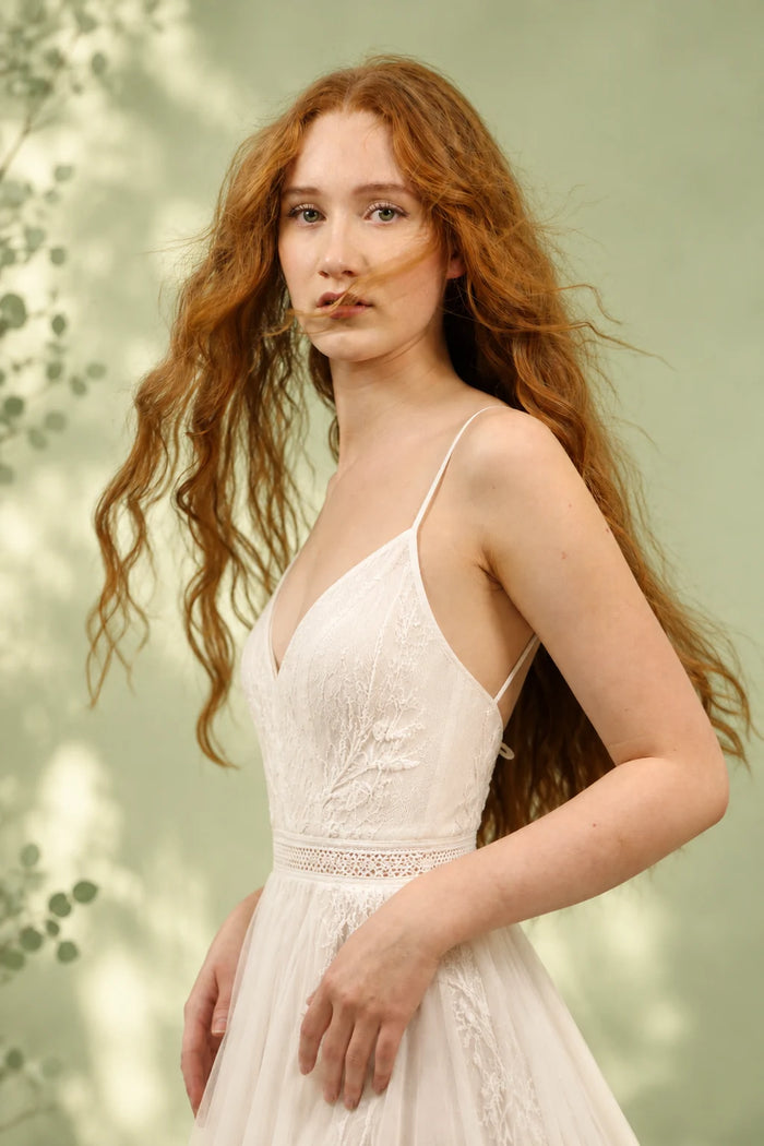 Bridal-mit Model und langen natürlichen roten Haaren. Das Model trägt ein rückenfreies Boho-Brautkleid mit feinen Spaghettiträgern. Natürliches Make-up, helle Haut und weiches Tageslicht vor einem pastellgrünen Hintergrund verleihen dem Bild einen romantischen, zeitlosen und eleganten Braut-Look.