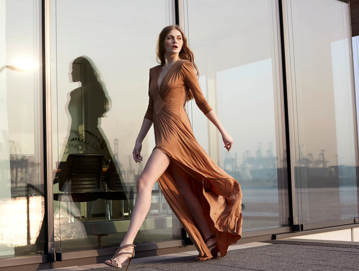 fashion-Aufnahme im Hamburger Hafen: Model im fließenden kupferfarbenen Abendkleid  von Elisabetta Franchi vor Glasfassade. 