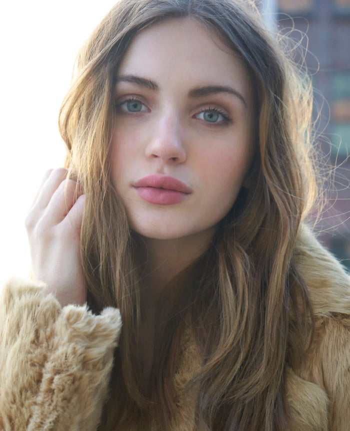 Fashion-Beauty-Porträt von Model Isa mit langen offenen Haaren, natürlichem Make-up und sinnlichem Blick. Die beigefarbene Felljacke, das weiche Gegenlicht und die sanften Farben schaffen einen romantischen, modernen und zeitlosen Fashion-Look.