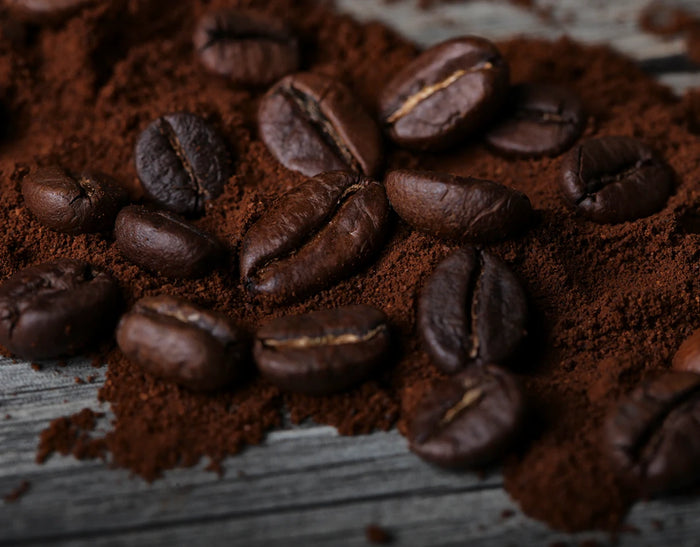 Makro-Still-Life von gerösteten Kaffeebohnen und aromatischem Kaffeepulver auf heller Holzoberfläche. Detailreiche Produktfotografie für Espresso, Kaffee, Kaffeerösterei und italienische Genusskultur.