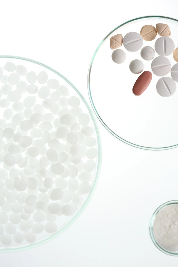 Still-Life-Aufnahme verschiedener Tabletten und Kapseln auf transparenten Glasschalen. Minimalistisches Labormotiv für Pharma, Hautpflege, Kosmetik und wissenschaftliche Produktentwicklung.
