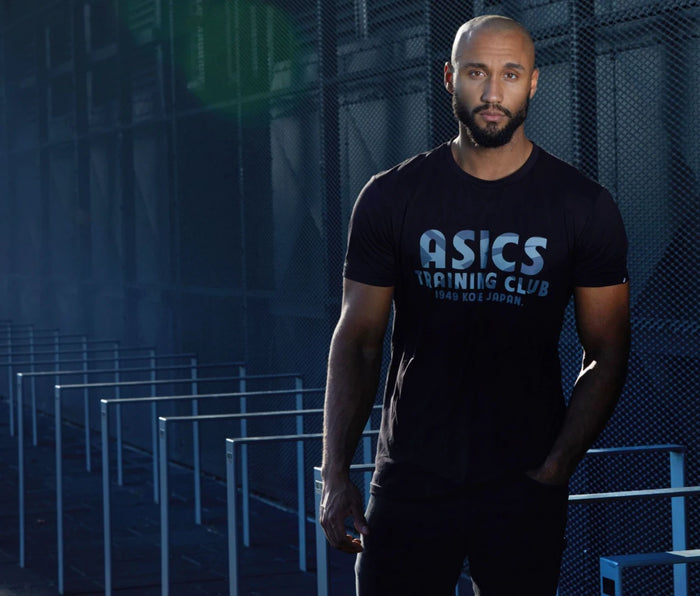 Athletisches Männermodel im schwarzen ASICS Training Club T-Shirt am Hamburger Hafen. Sport- und Fitness-Fashion mit modernem Industrie-Look, markantem Gegenlicht und urbaner Atmosphäre. Kraftvolle Sportfotografie für Activewear und Lifestyle.