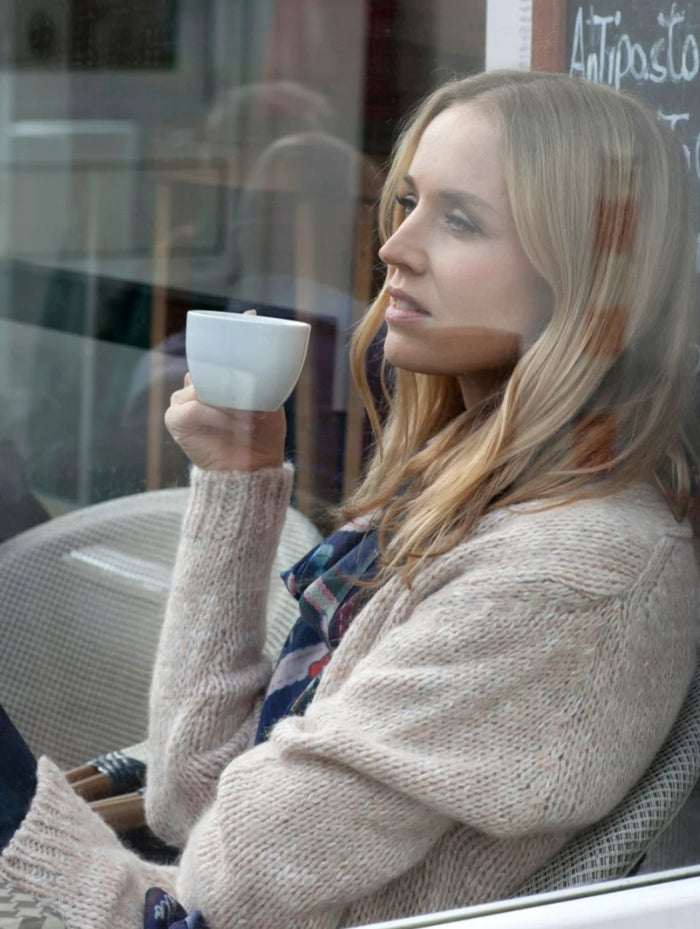 Portrait einer blonden Frau mit Espressotasse am Caféfenster.